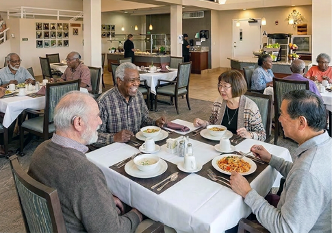 A group of elderly people are sitting in a restaurant, enjoying their meal. They are seated at tables with chairs, and some of them are using cell phones. The restaurant has a cozy atmosphere with a couch and a TV in the background. AI generated content